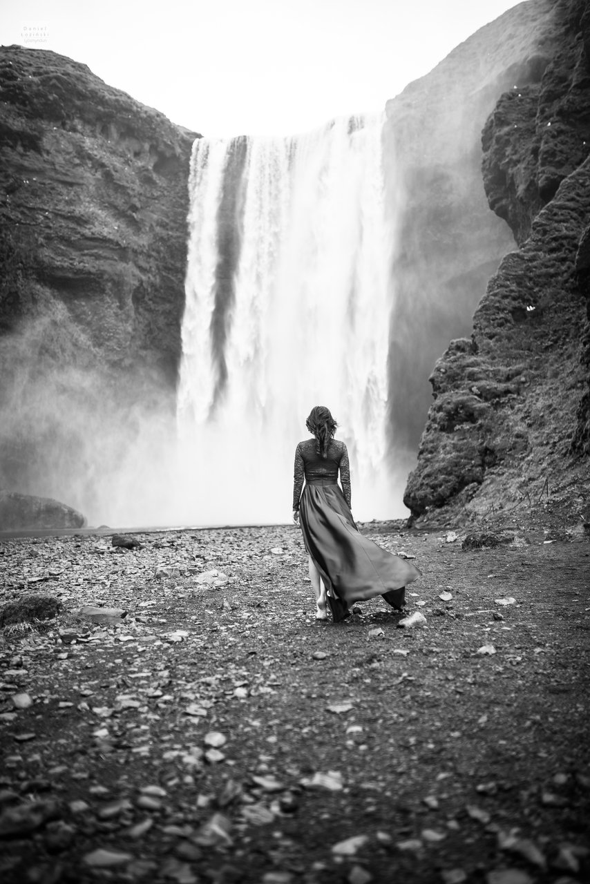 Myndataka af konu í rauðum kjól við fossinn Skógafoss á Íslandi (Golden Circle). Svarthvítar myndir. Ljósmynd tekin af ljósmyndaranum Daniel Łoziński með Nikon D850 myndavélinni og Sigma linsum, ART röð.