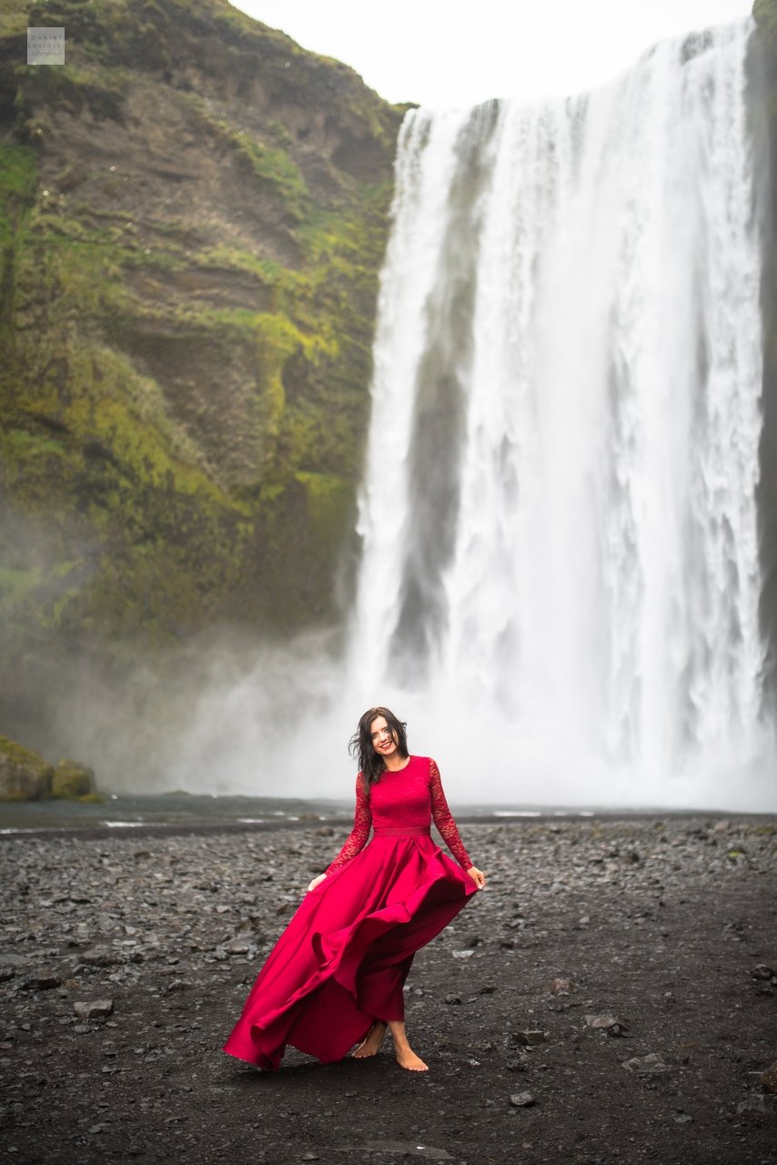 Myndataka af konu í rauðum kjól við fossinn Skógafoss á Íslandi (Golden Circle). Ljósmynd tekin af ljósmyndaranum Daniel Łoziński með Nikon D850 myndavélinni og Sigma linsum, ART röð.